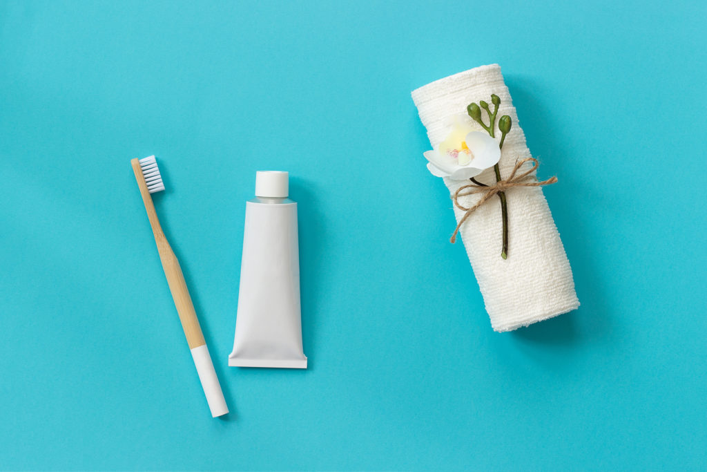 Naturalna biała pasta do zębów na szczoteczce. Biały ręcznik, wstążka, roślinka, kwiat.